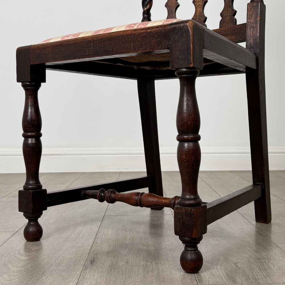 A set of four dark oak dining chairs with barley twist side supports, carved top crests, vertically slatted backrests, and striped fabric seat cushions. View V