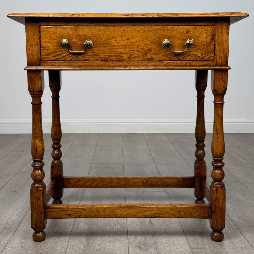 A golden oak side table featuring a single drawer with two brass handles, turned legs, and an lower stretcher base.