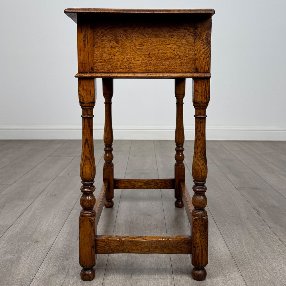 A golden oak side table featuring a single drawer with two brass handles, turned legs, and an lower stretcher base. View III