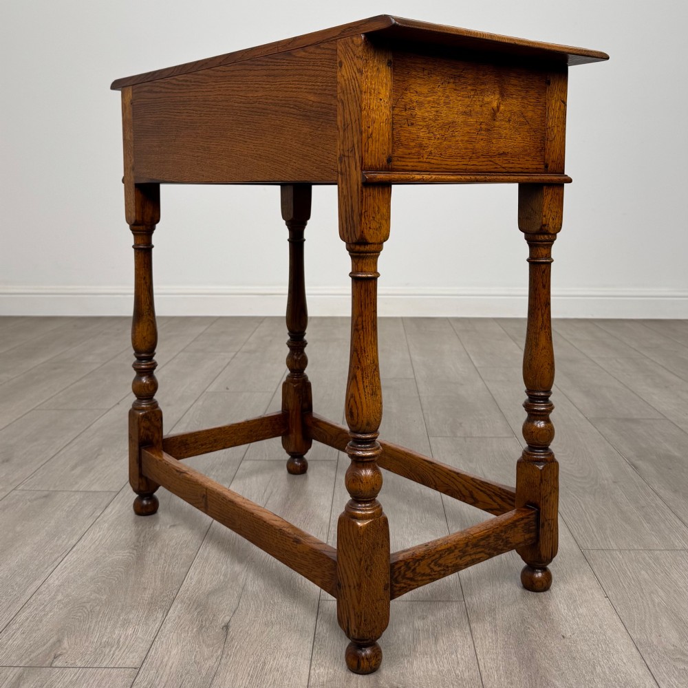 A golden oak side table featuring a single drawer with two brass handles, turned legs, and an lower stretcher base. View VI