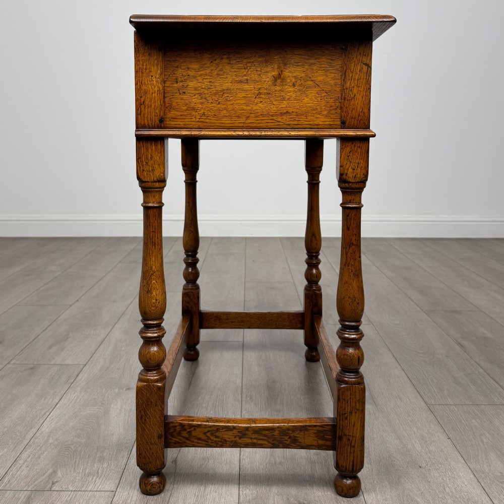 A golden oak side table featuring a single drawer with two brass handles, turned legs, and an lower stretcher base. View VII
