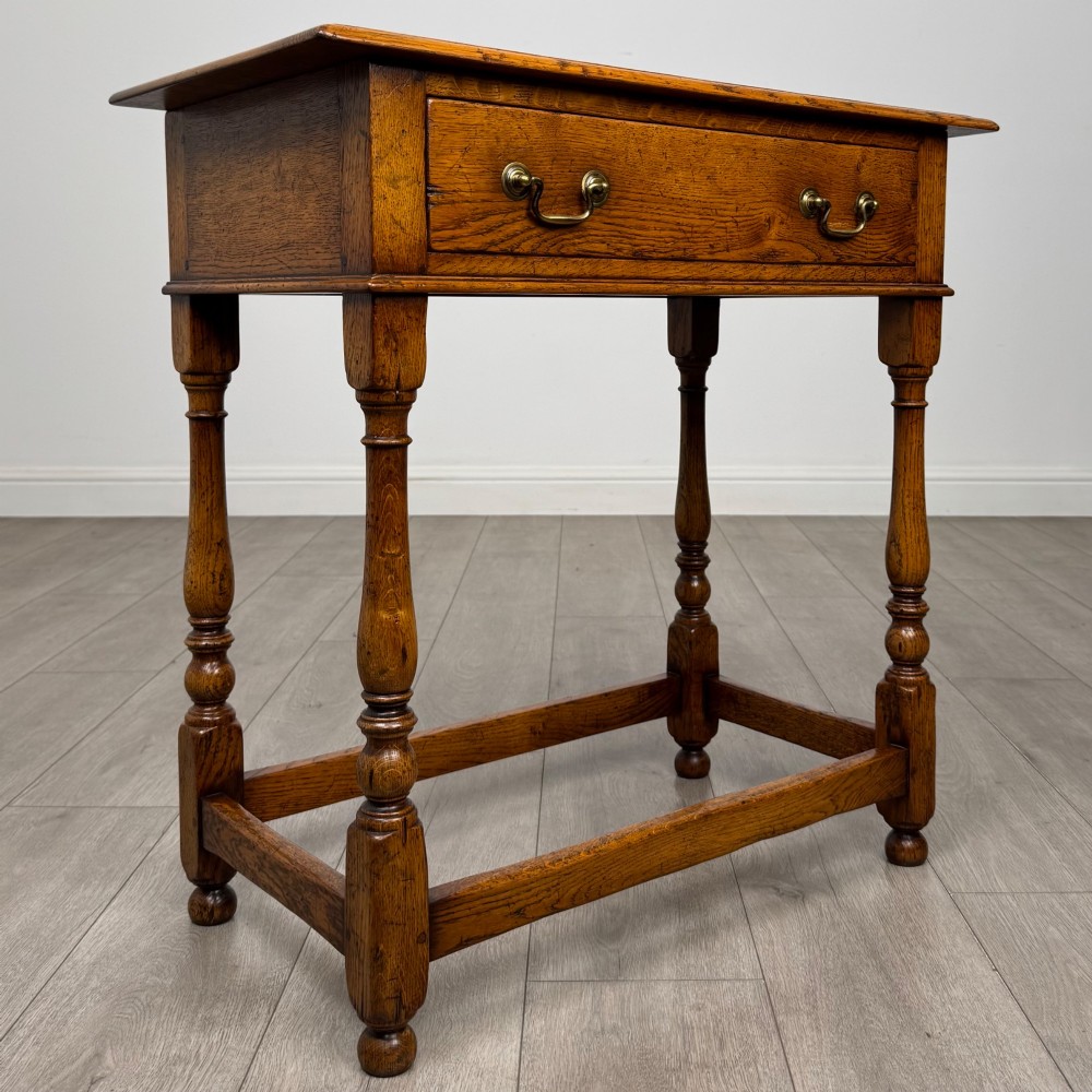 A golden oak side table featuring a single drawer with two brass handles, turned legs, and an lower stretcher base. View VIII