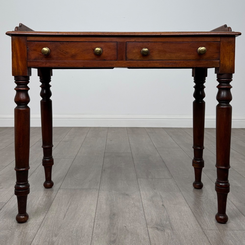 A Victorian mahogany writing table featuring two frieze drawers with brass knob handles, turned legs, and a low gallery back.