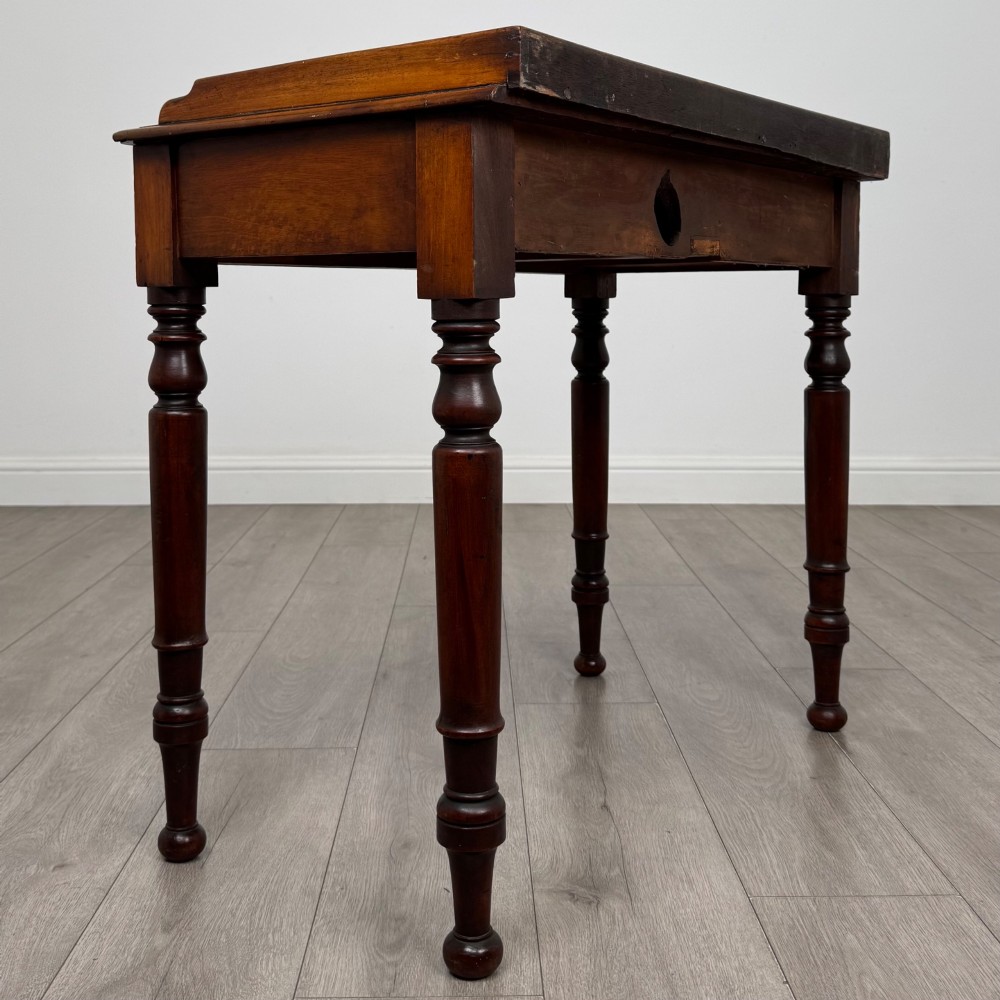 A Victorian mahogany writing table featuring two frieze drawers with brass knob handles, turned legs, and a low gallery back. View IV