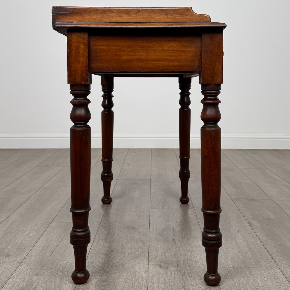 A Victorian mahogany writing table featuring two frieze drawers with brass knob handles, turned legs, and a low gallery back. View VII