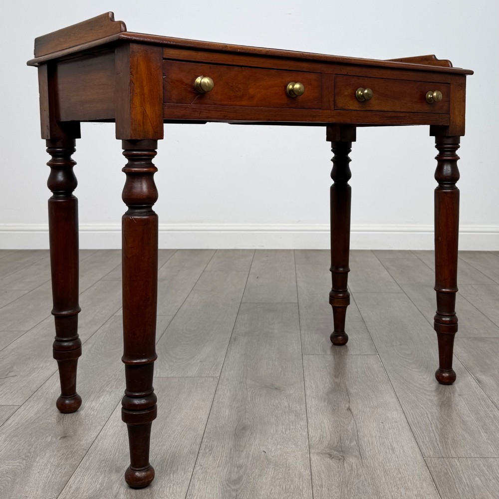 A Victorian mahogany writing table featuring two frieze drawers with brass knob handles, turned legs, and a low gallery back. View VIII