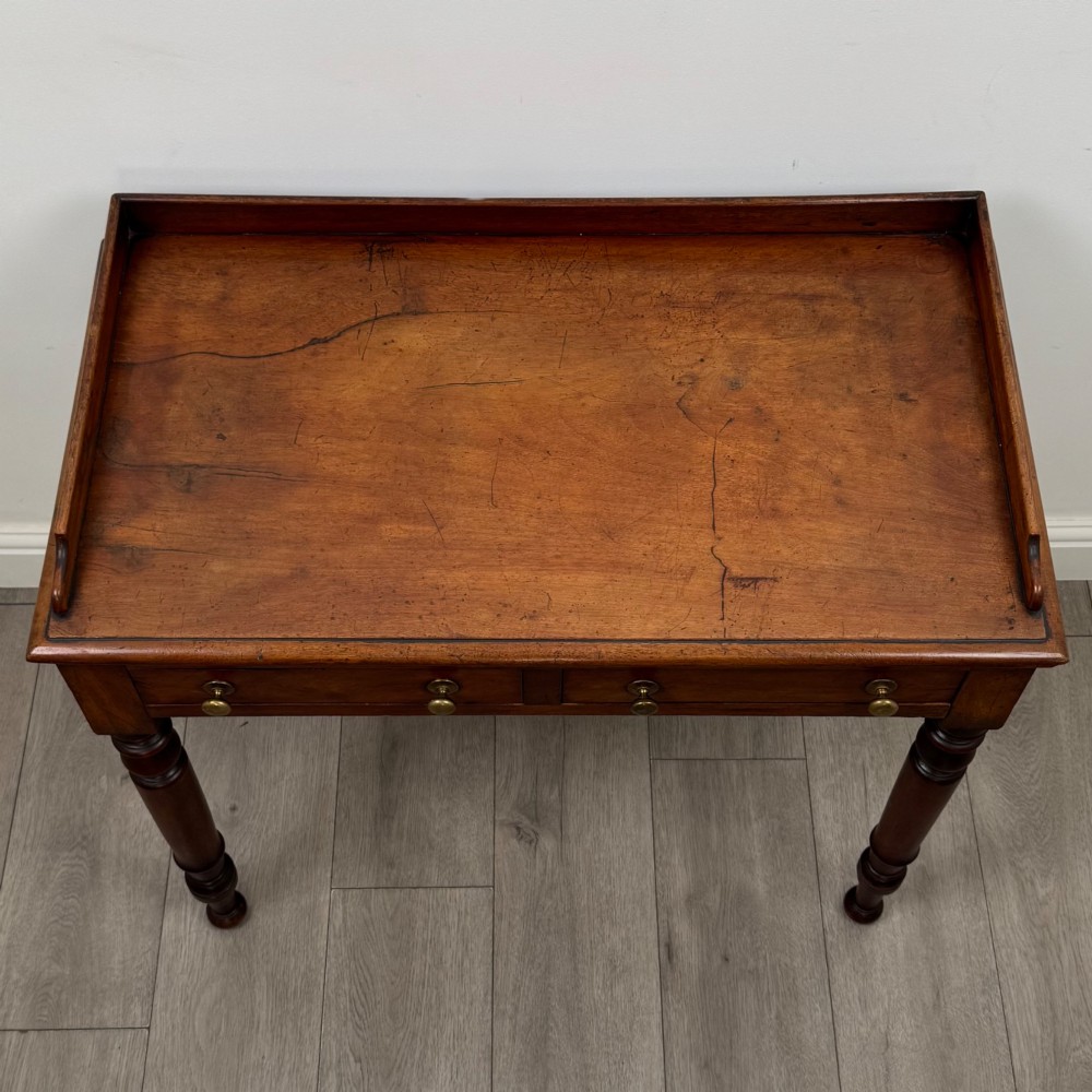 A Victorian mahogany writing table featuring two frieze drawers with brass knob handles, turned legs, and a low gallery back. View IX