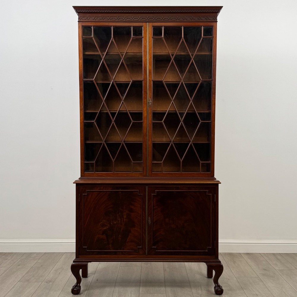 A 20th-century Chippendale style mahogany bookcase featuring two upper glazed doors with diamond pattern astragal glazing and a two-door cupboard base raised on cabriole legs with claw and ball feet.