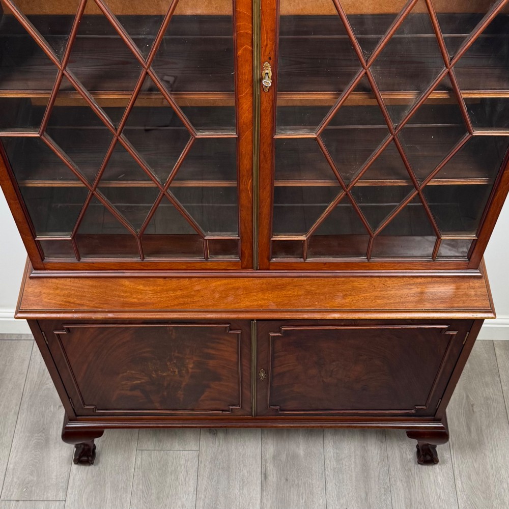 A 20th-century Chippendale style mahogany bookcase featuring two upper glazed doors with diamond pattern astragal glazing and a two-door cupboard base raised on cabriole legs with claw and ball feet. View X