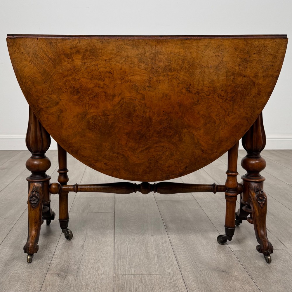 A 19th-century Victorian Sutherland table crafted from burr walnut featuring folded drop leaves, turned twin-column supports, and carved legs on brass castors. View II