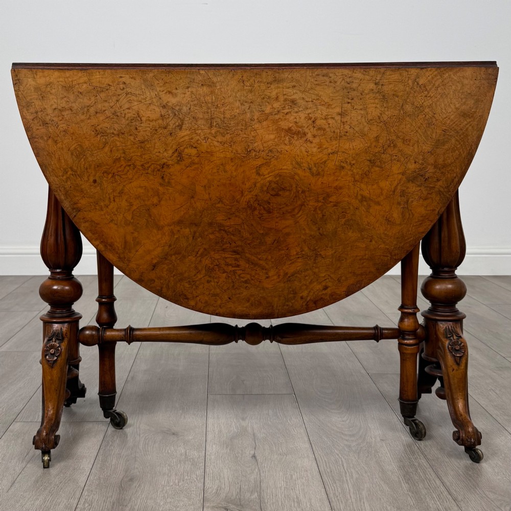 A 19th-century Victorian Sutherland table crafted from burr walnut featuring folded drop leaves, turned twin-column supports, and carved legs on brass castors. View VII