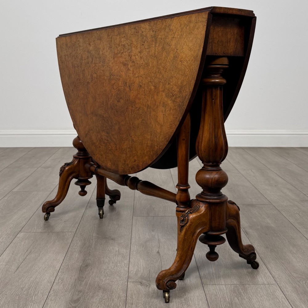 A 19th-century Victorian Sutherland table crafted from burr walnut featuring folded drop leaves, turned twin-column supports, and carved legs on brass castors. View VIII