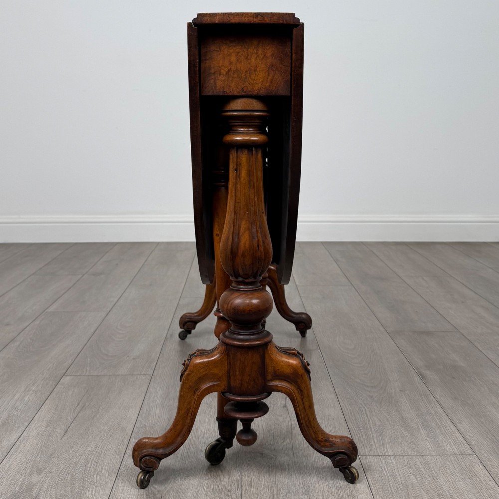 A 19th-century Victorian Sutherland table crafted from burr walnut featuring folded drop leaves, turned twin-column supports, and carved legs on brass castors. View IX