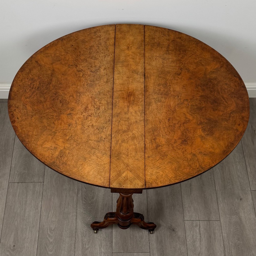 A 19th-century Victorian Sutherland table crafted from burr walnut featuring folded drop leaves, turned twin-column supports, and carved legs on brass castors. View XI