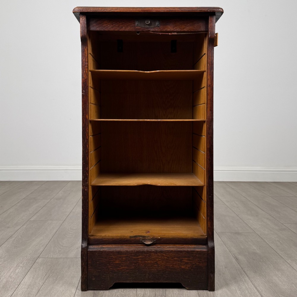 An antique dark oak tambour cabinet featuring a vertical wooden slat roll-front door and top brass locking mechanism. View II