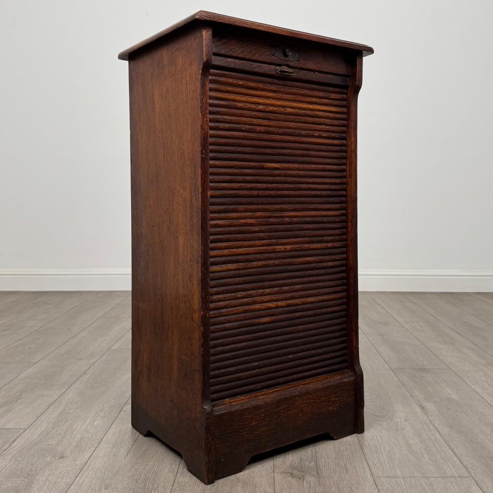 An antique dark oak tambour cabinet featuring a vertical wooden slat roll-front door and top brass locking mechanism. View IX