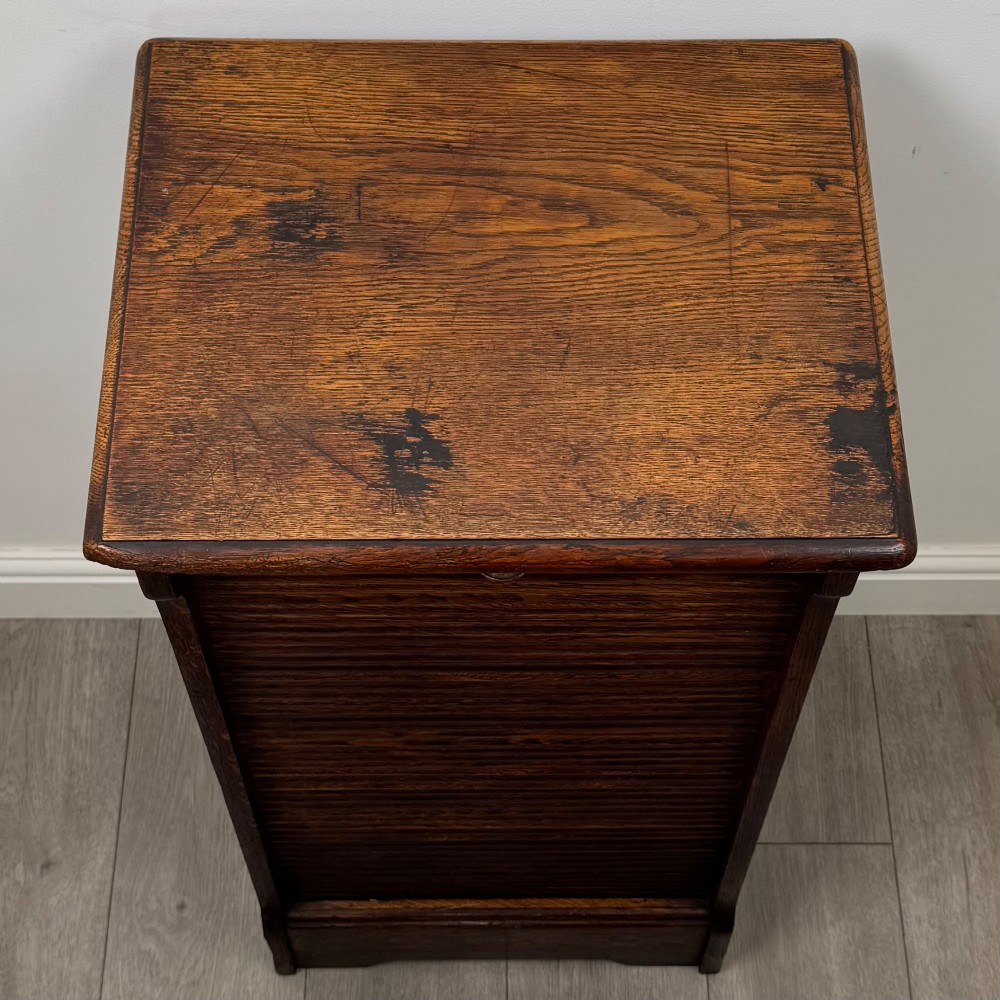 An antique dark oak tambour cabinet featuring a vertical wooden slat roll-front door and top brass locking mechanism. View X