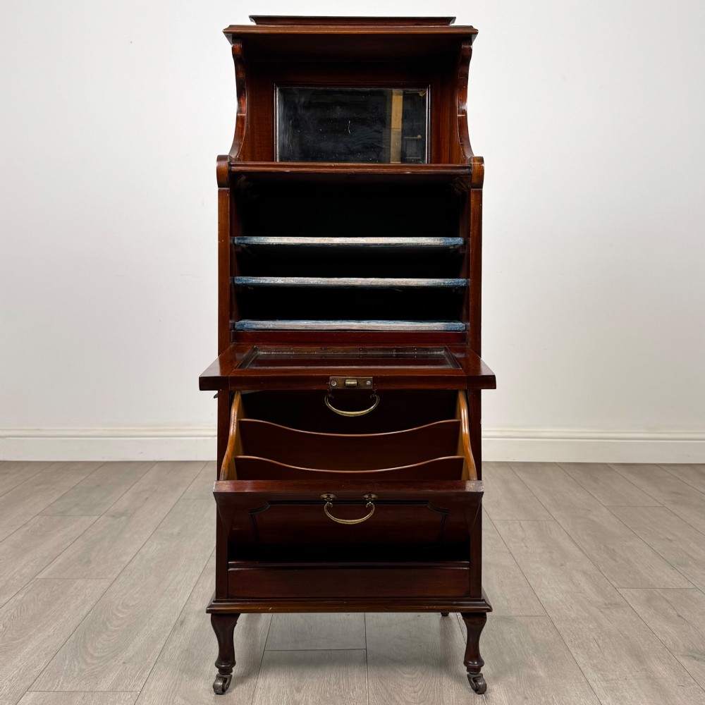 An early 20th-century mahogany music cabinet with an upper mirrored shelf, a middle glazed drawer compartment, a lower moulded panel door, and brass handles on castors. View II