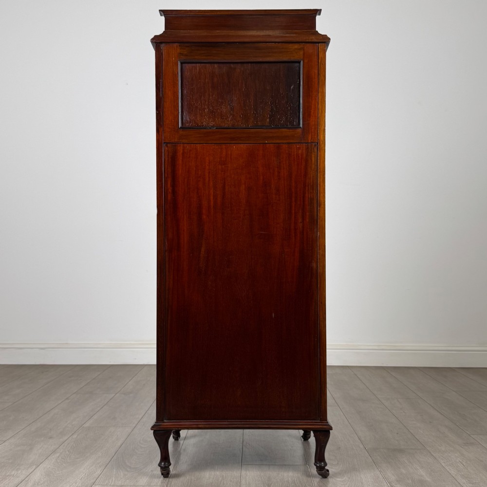 An early 20th-century mahogany music cabinet with an upper mirrored shelf, a middle glazed drawer compartment, a lower moulded panel door, and brass handles on castors. View VI