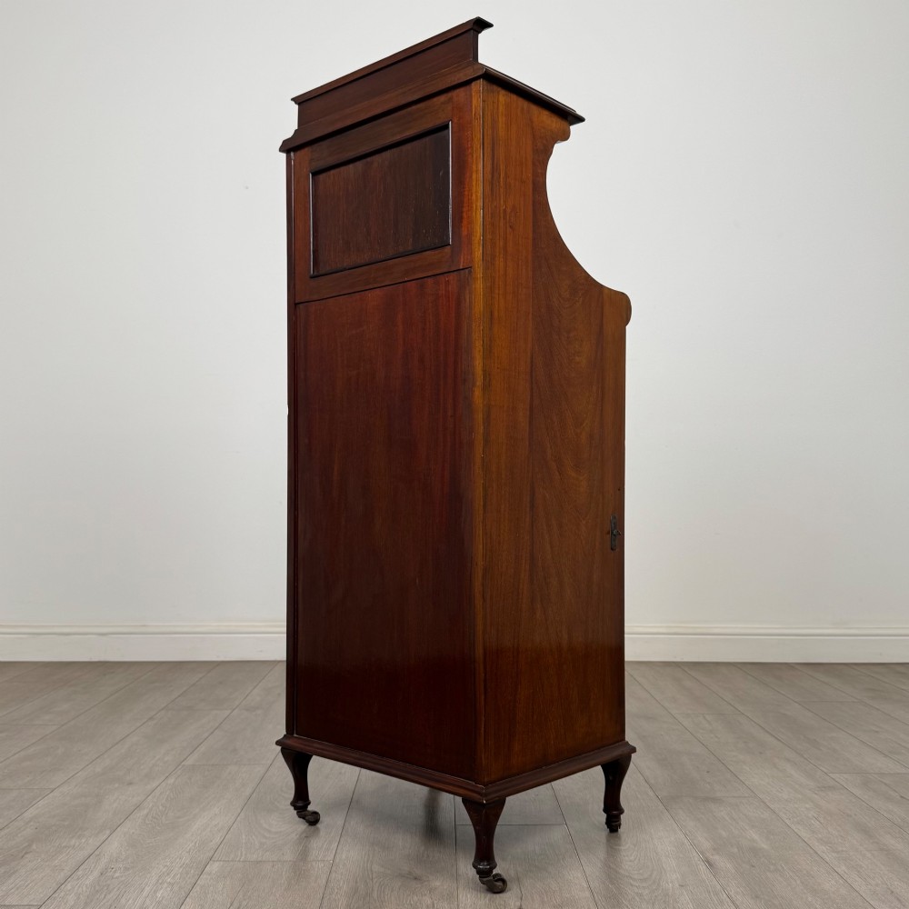 An early 20th-century mahogany music cabinet with an upper mirrored shelf, a middle glazed drawer compartment, a lower moulded panel door, and brass handles on castors. View VII