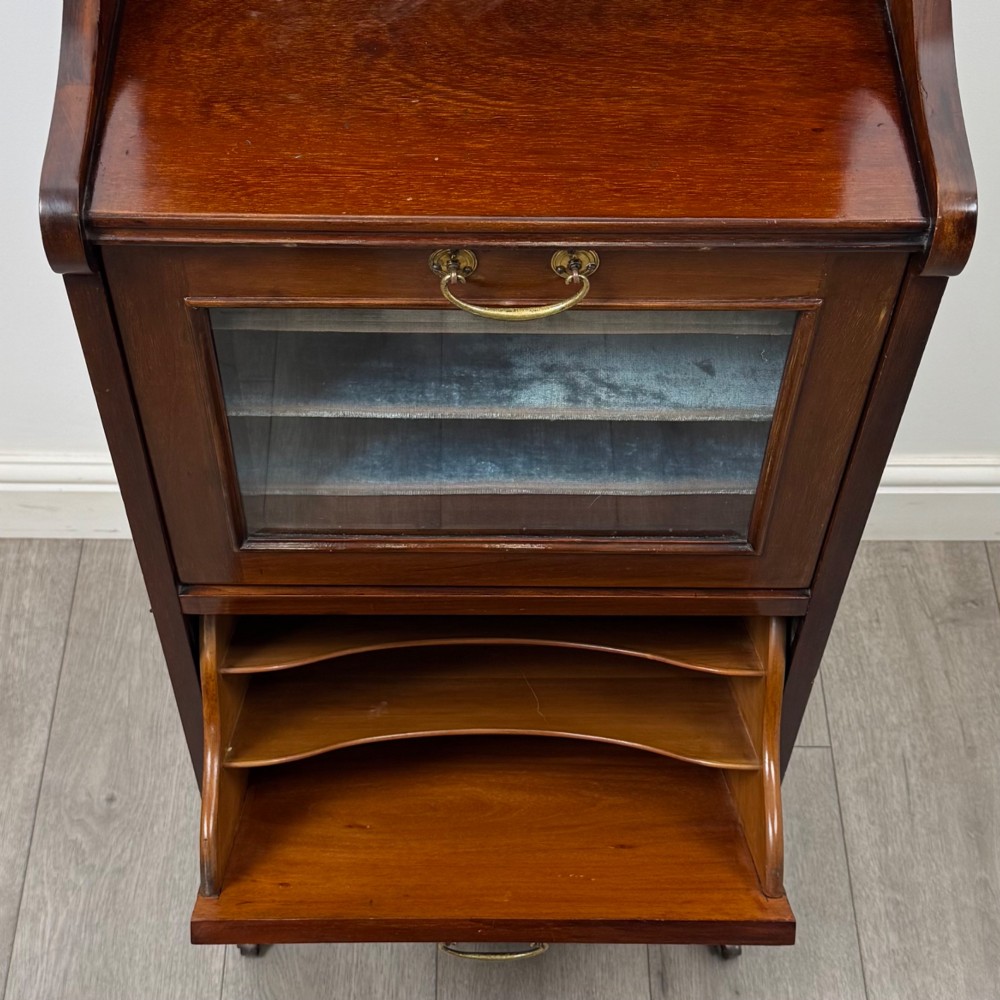 An early 20th-century mahogany music cabinet with an upper mirrored shelf, a middle glazed drawer compartment, a lower moulded panel door, and brass handles on castors. View XI