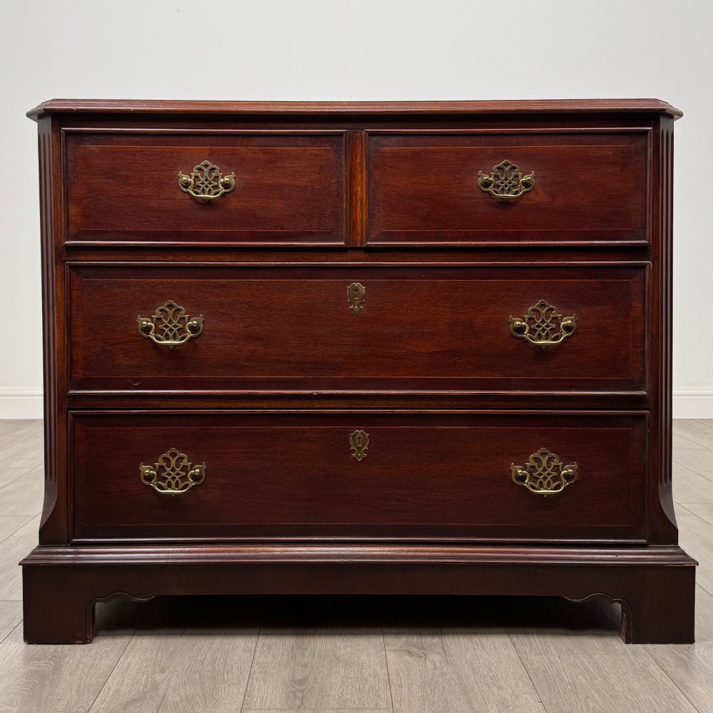 A 20th-century American mahogany chest of drawers featuring two small top drawers, two full-width lower drawers, brass bail handles, fluted quarter-columns, and bracket feet.
