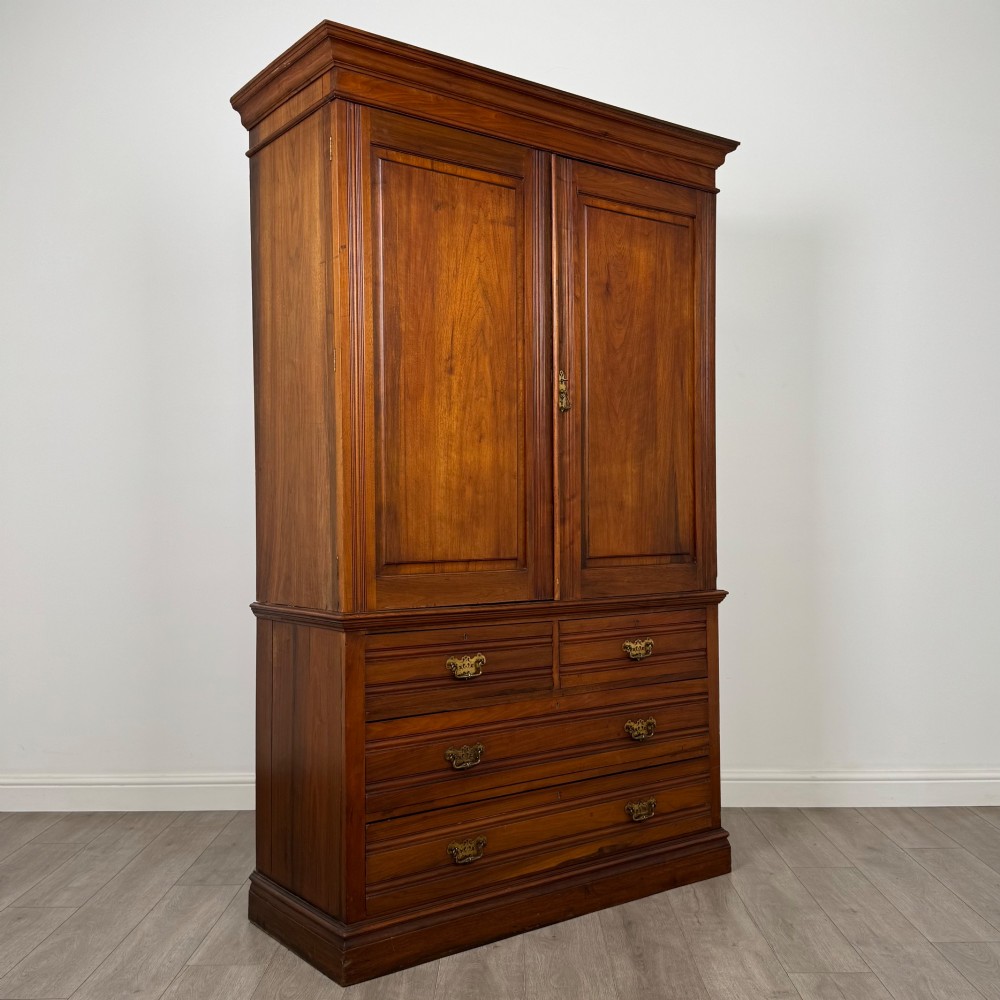 An Edwardian walnut linen press featuring a moulded top cornice, two large upper recessed panel doors, and a lower chest of drawers with brass drop handles. View IX