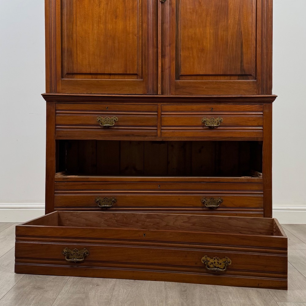 An Edwardian walnut linen press featuring a moulded top cornice, two large upper recessed panel doors, and a lower chest of drawers with brass drop handles. View X