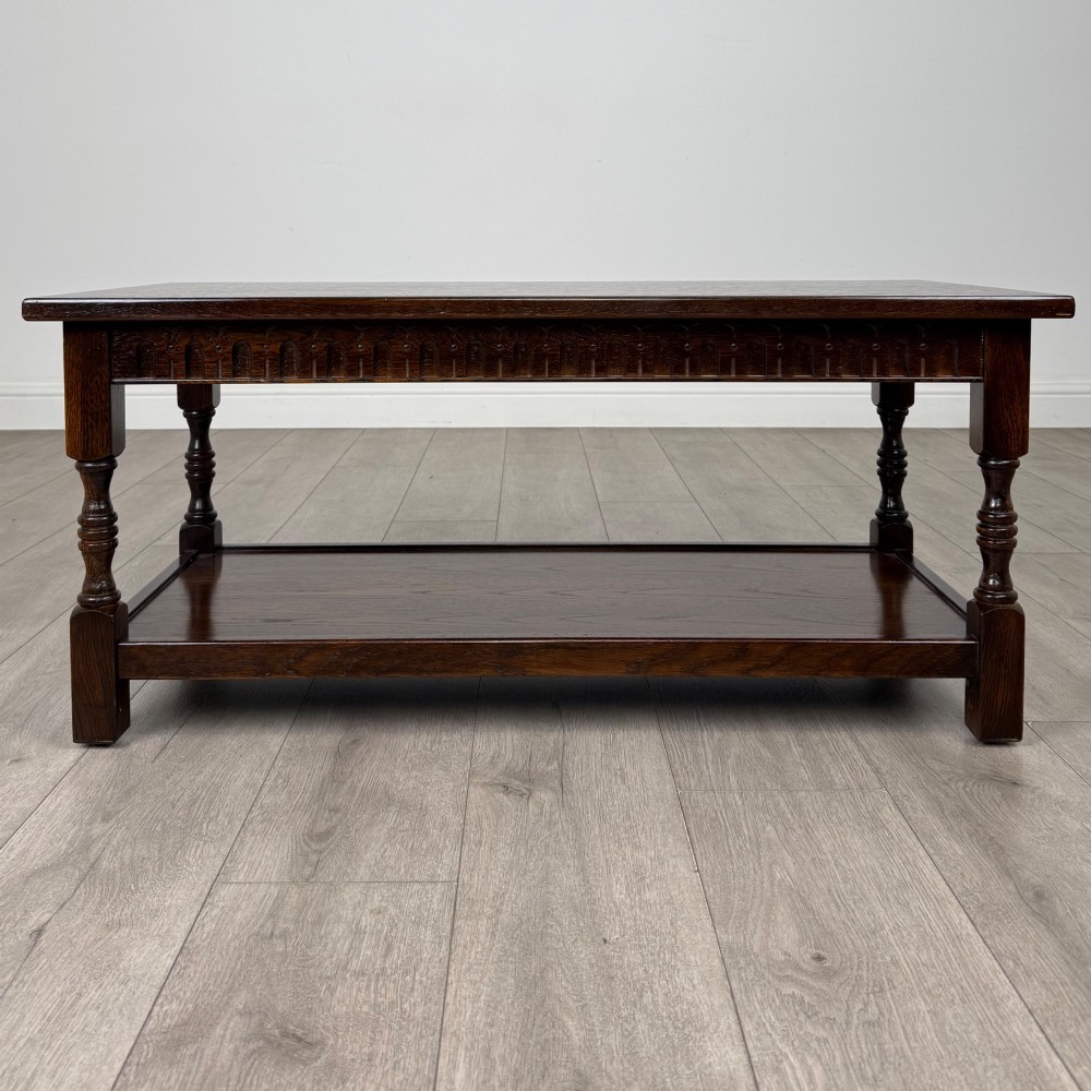 A dark carved oak coffee table featuring an arcaded carved apron, turned legs, and an integrated lower shelf.