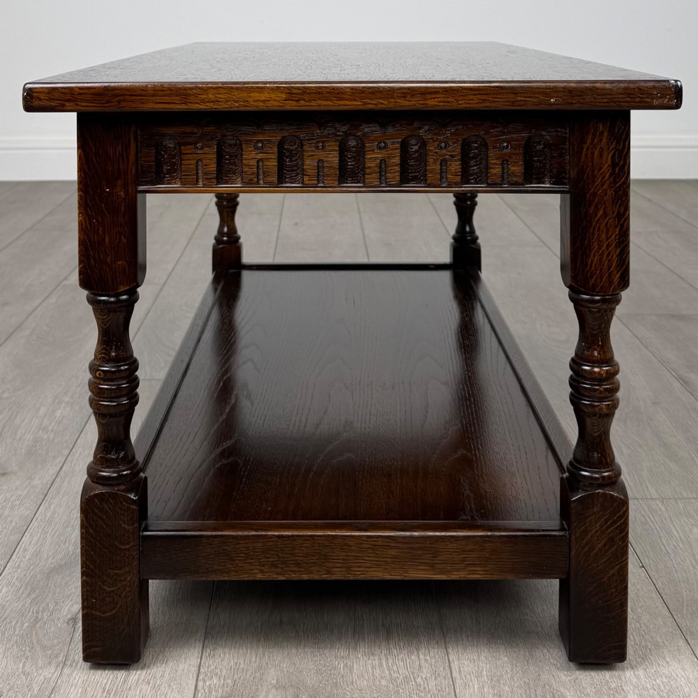 A dark carved oak coffee table featuring an arcaded carved apron, turned legs, and an integrated lower shelf. View III