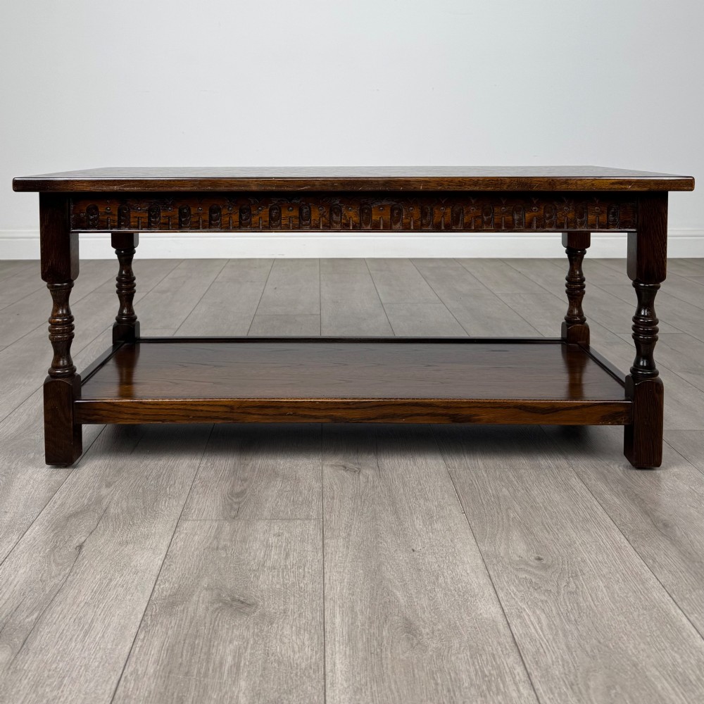 A dark carved oak coffee table featuring an arcaded carved apron, turned legs, and an integrated lower shelf. View IV