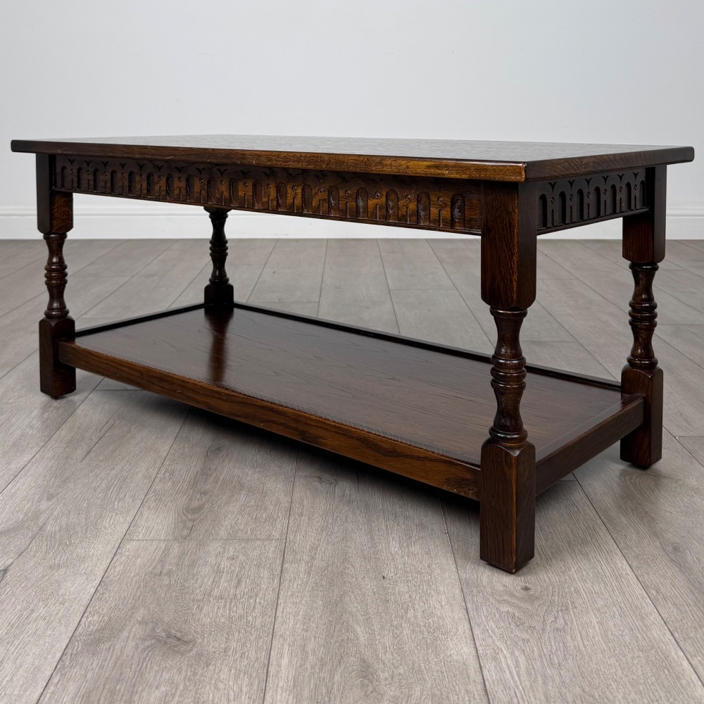 A dark carved oak coffee table featuring an arcaded carved apron, turned legs, and an integrated lower shelf. View V