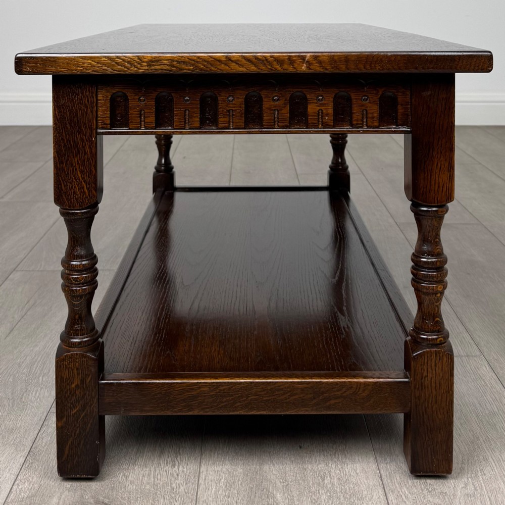 A dark carved oak coffee table featuring an arcaded carved apron, turned legs, and an integrated lower shelf. View VI
