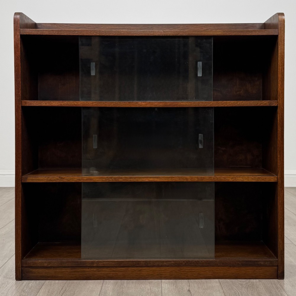 A mid-twentieth-century dark oak display cabinet featuring three interior shelf tiers enclosed by sliding glass doors. View II