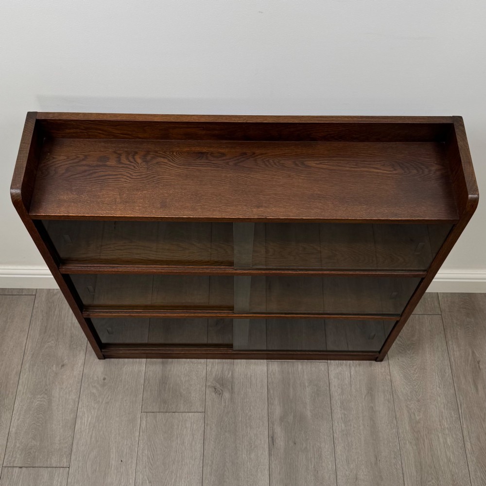 A mid-twentieth-century dark oak display cabinet featuring three interior shelf tiers enclosed by sliding glass doors. View X