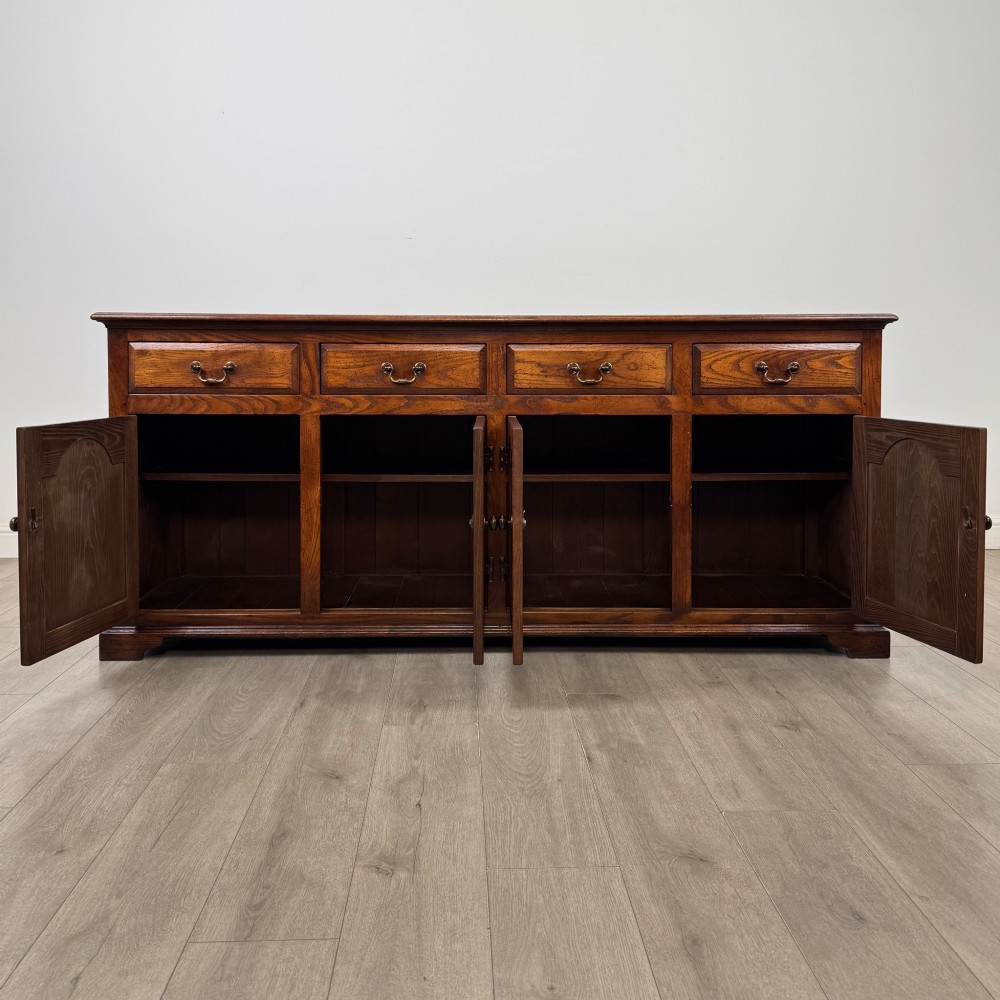 A large medium brown oak sideboard featuring four upper drawers with brass handles above four cupboard doors with arched wood panels. View II