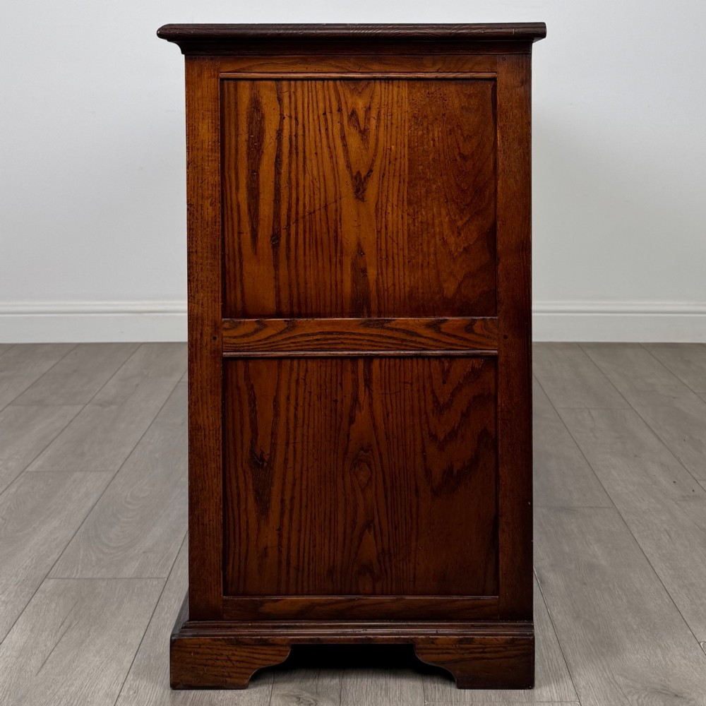 A large medium brown oak sideboard featuring four upper drawers with brass handles above four cupboard doors with arched wood panels. View IV