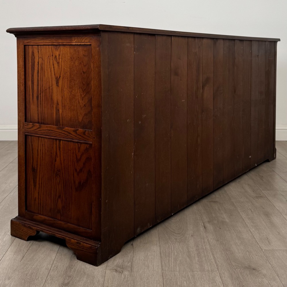 A large medium brown oak sideboard featuring four upper drawers with brass handles above four cupboard doors with arched wood panels. View V