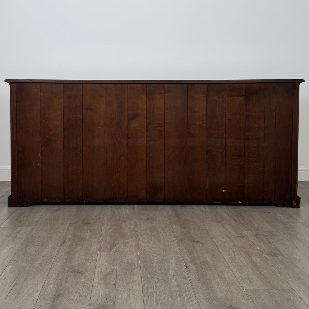 A large medium brown oak sideboard featuring four upper drawers with brass handles above four cupboard doors with arched wood panels. View VI