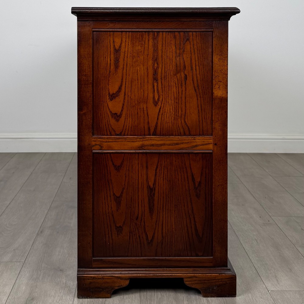 A large medium brown oak sideboard featuring four upper drawers with brass handles above four cupboard doors with arched wood panels. View VIII