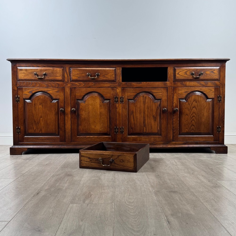 A large medium brown oak sideboard featuring four upper drawers with brass handles above four cupboard doors with arched wood panels. View XI