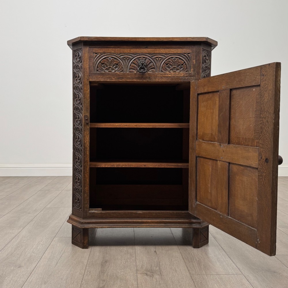 A small dark oak cupboard featuring a single carved top drawer above a panelled cupboard door with iron hinges. View II