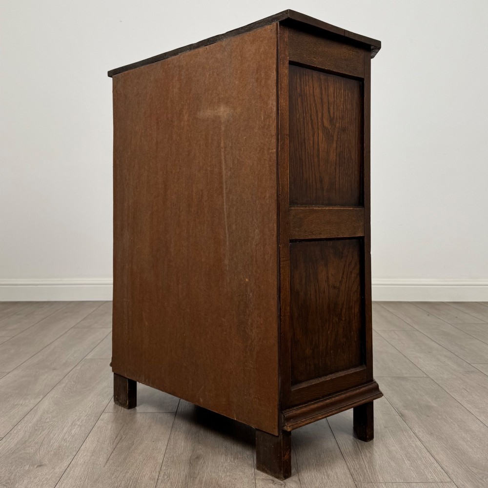 A small dark oak cupboard featuring a single carved top drawer above a panelled cupboard door with iron hinges. View VII
