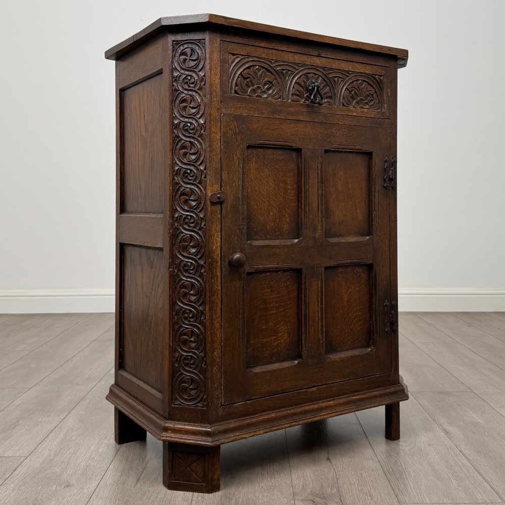 A small dark oak cupboard featuring a single carved top drawer above a panelled cupboard door with iron hinges. View IX