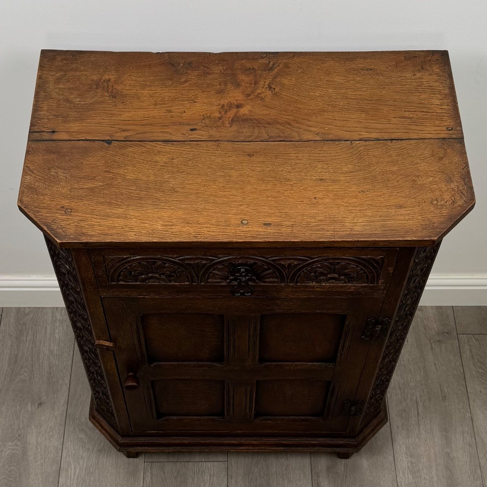 A small dark oak cupboard featuring a single carved top drawer above a panelled cupboard door with iron hinges. View X