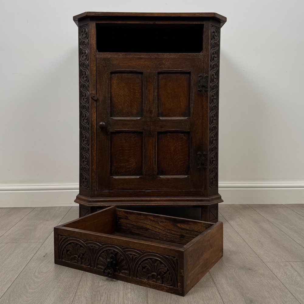 A small dark oak cupboard featuring a single carved top drawer above a panelled cupboard door with iron hinges. View XI