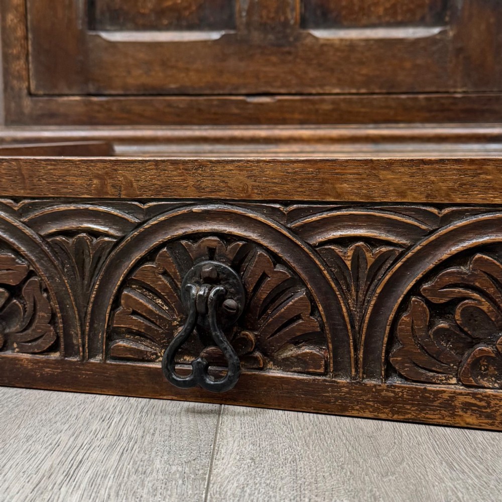 A small dark oak cupboard featuring a single carved top drawer above a panelled cupboard door with iron hinges. View XII