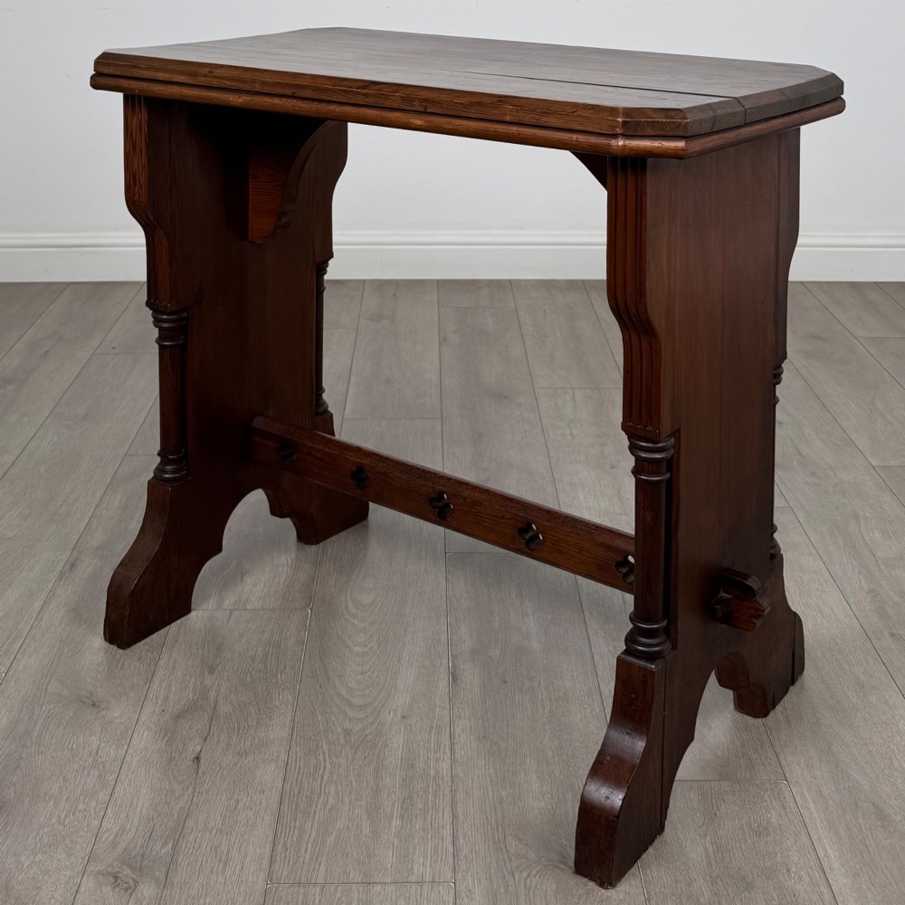 An antique 19th-century pitch pine side table featuring a Gothic Revival trestle base with turned column details and a pegged stretcher.
