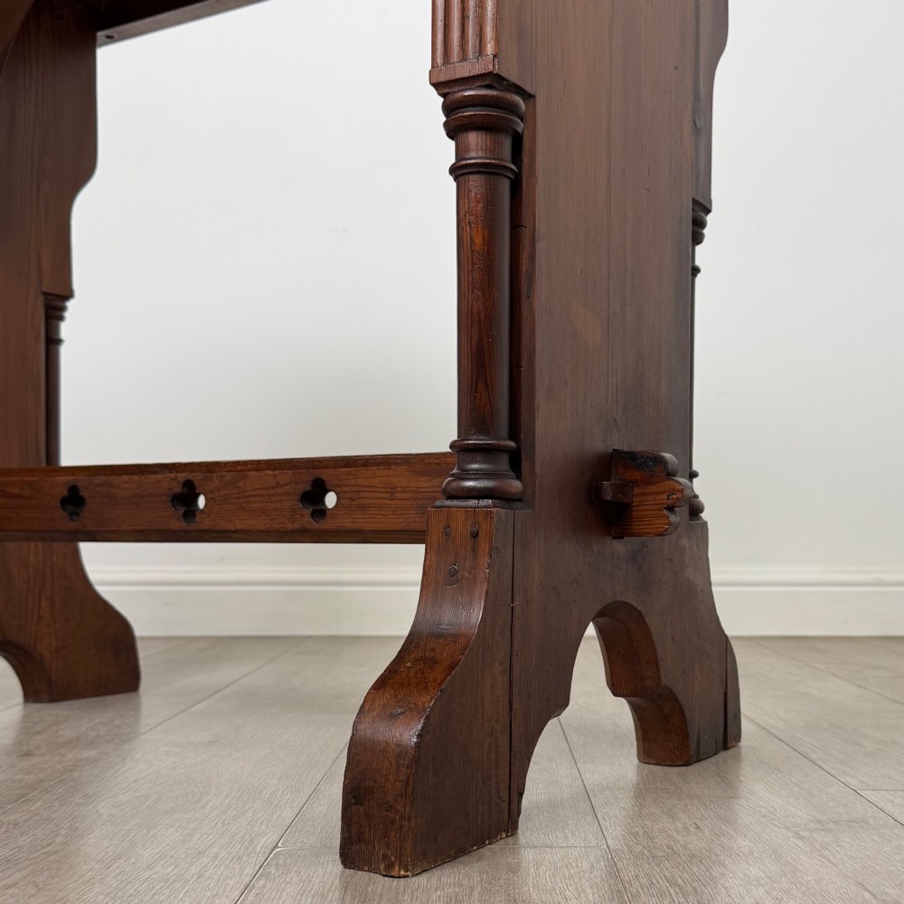 An antique 19th-century pitch pine side table featuring a Gothic Revival trestle base with turned column details and a pegged stretcher. View VI