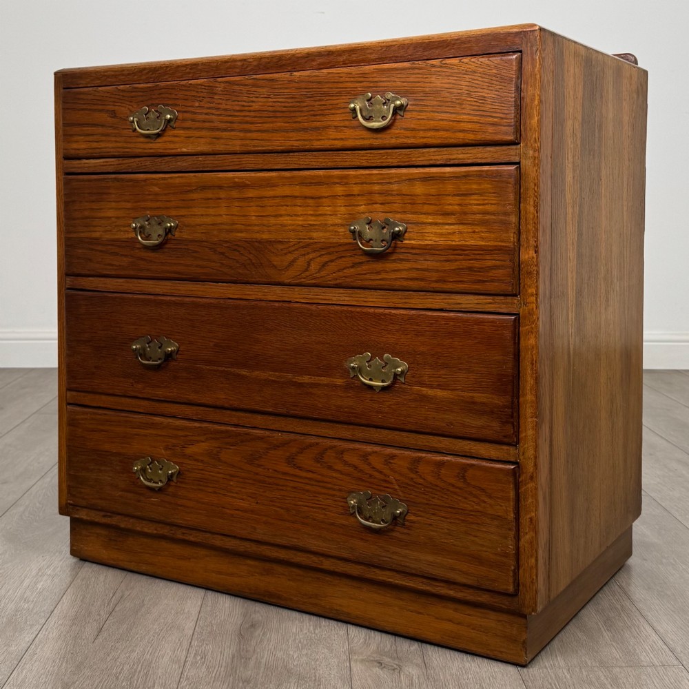 An antique golden oak chest of four drawers fitted with decorative brass drop handles on a plinth base. View II